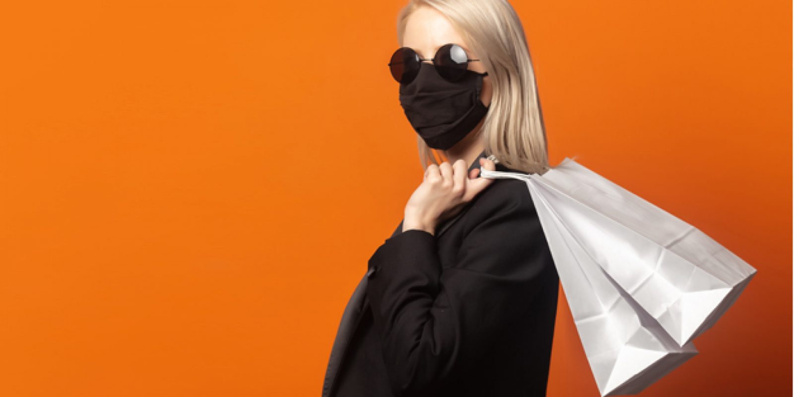 Style blonde in black blazer with shopping bags on an exuberant orange background